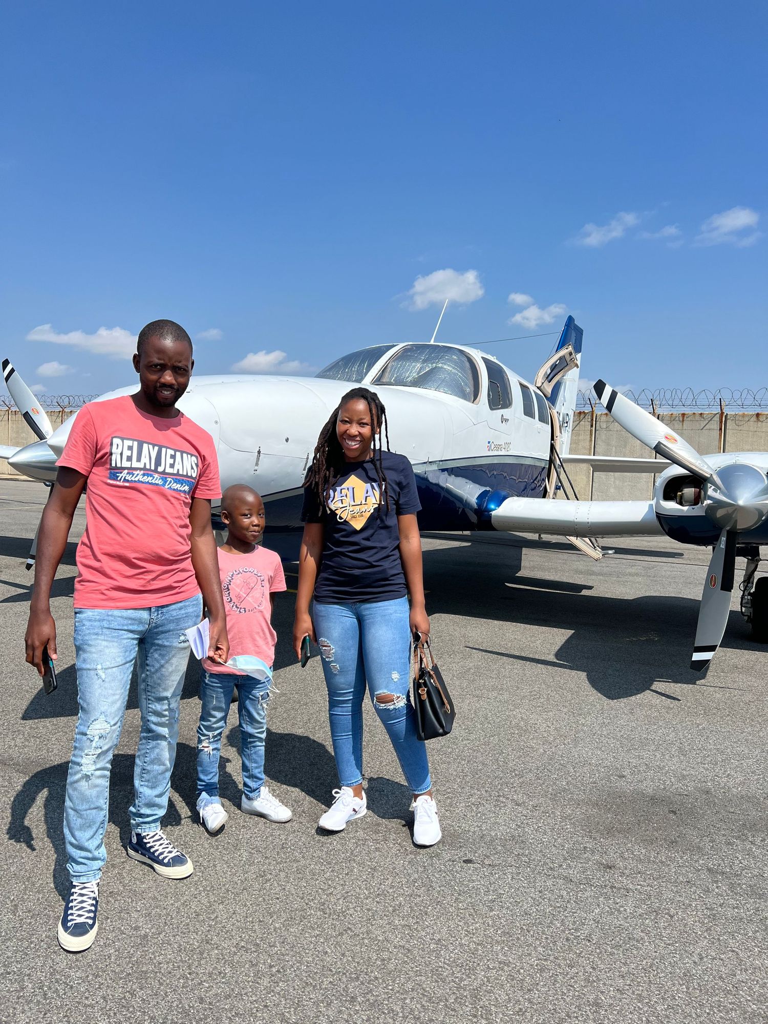 Group standing on airport tarmac next to parked small aircraft.