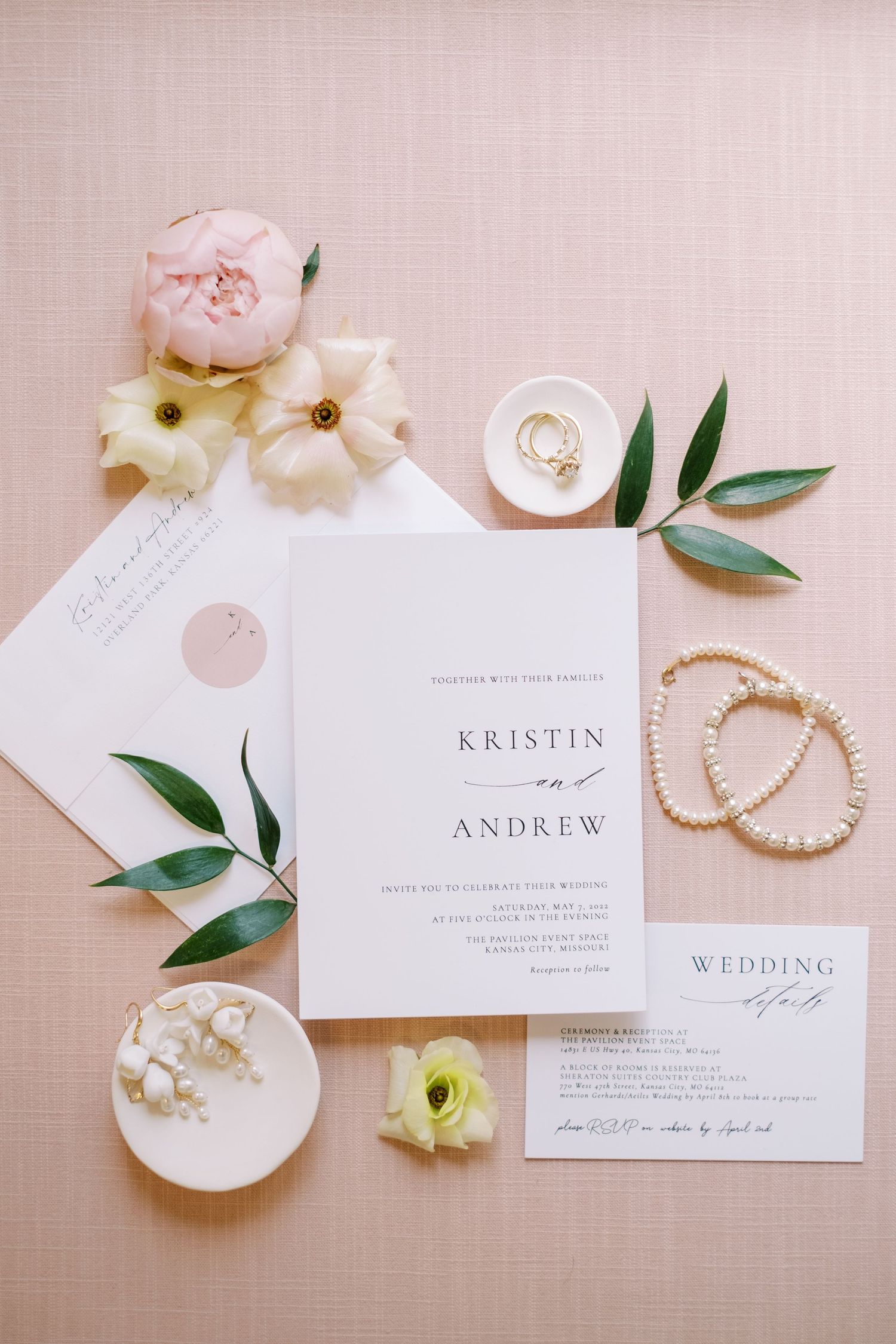 Wedding invitation suite with pearl jewelry and delicate floral accents on blush background.