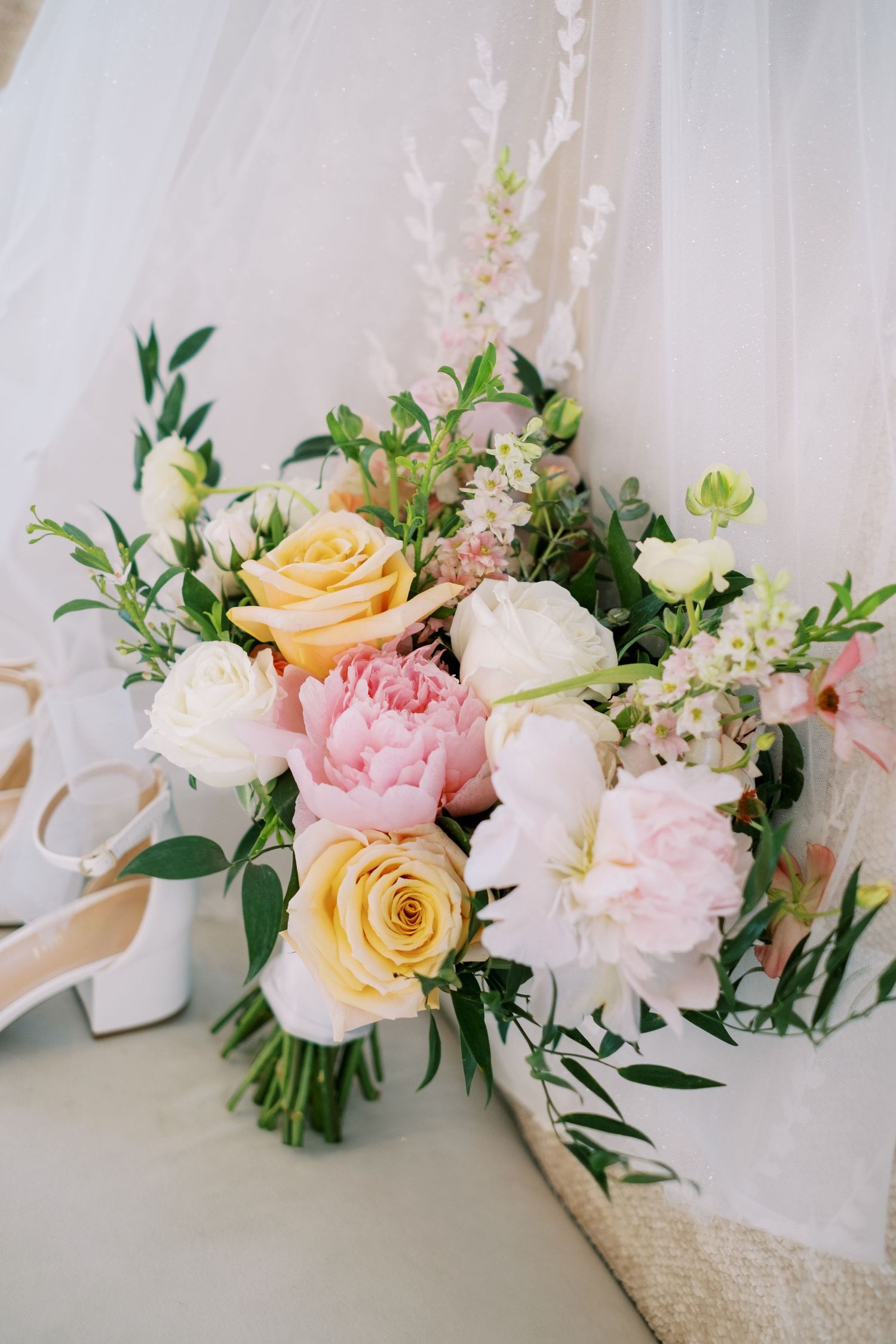 Romantic wedding bouquet featuring pink and yellow roses with white flowers and fresh greenery.