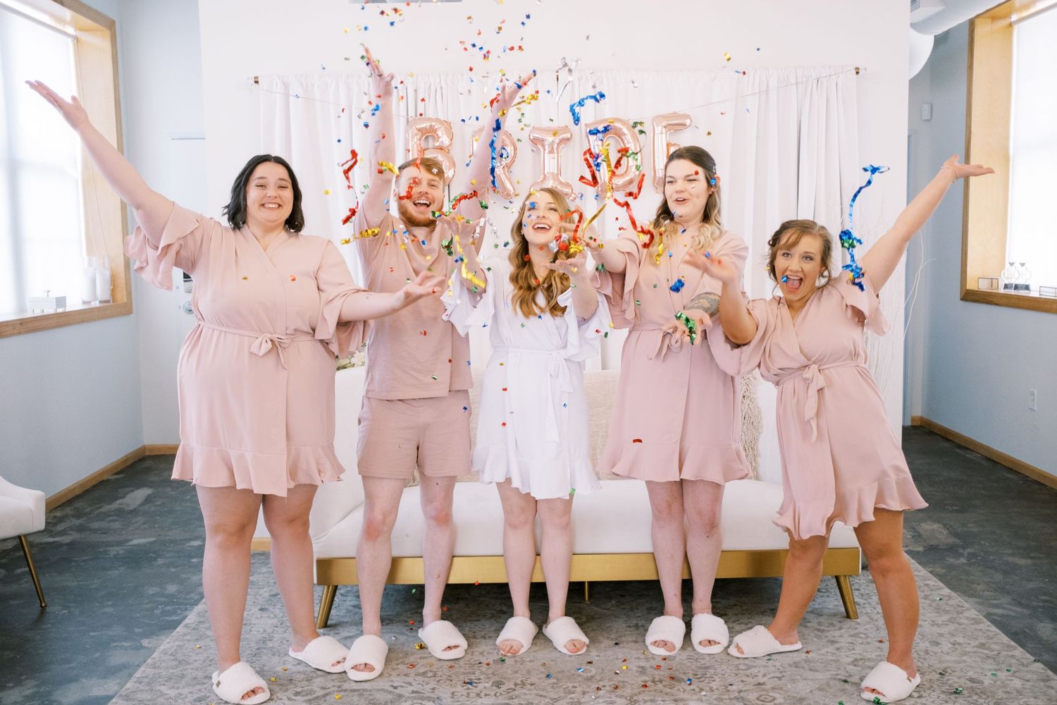 Bridesmaids in matching pink outfits celebrate joyfully in a hallway.