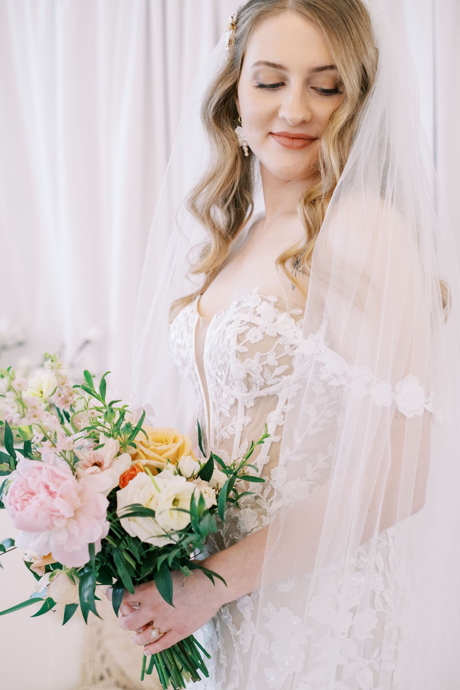 Delicate pastel bridal bouquet with roses and greenery against white background.
