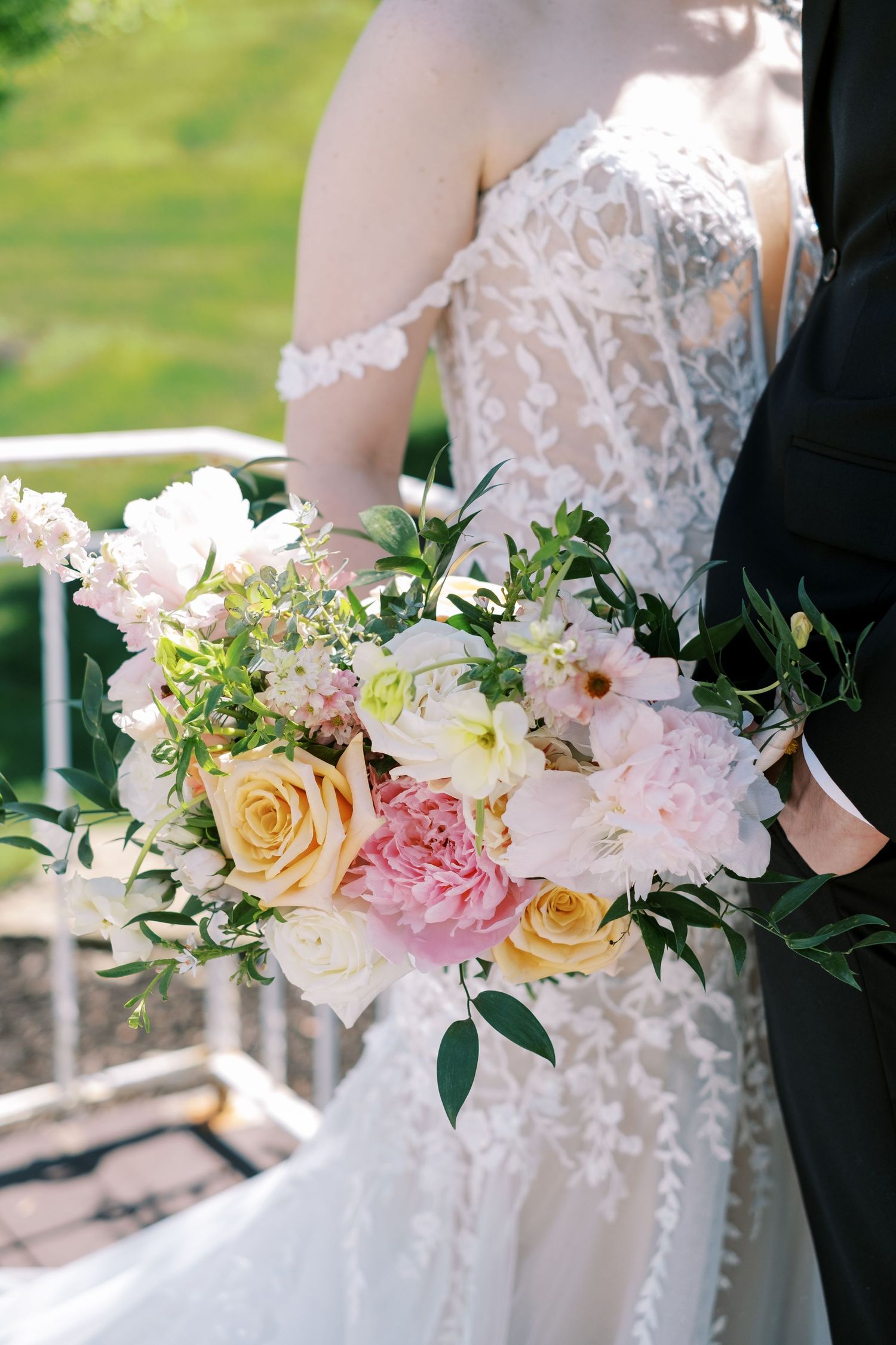 Close-up of bridal bouquet with pink and peach roses against a lace wedding dress.