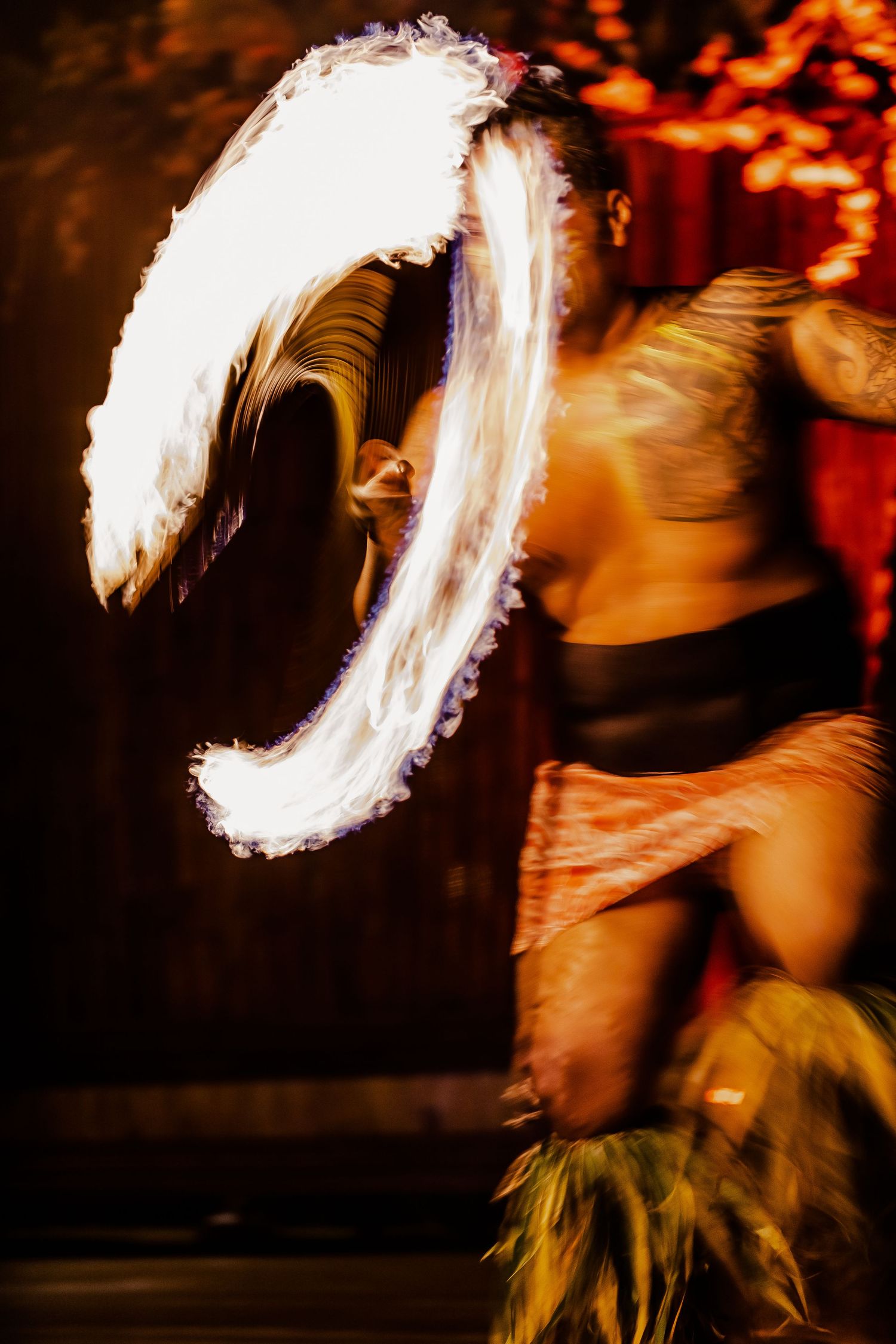 Fire dancer performing with glowing flame trails in dramatic nighttime show.