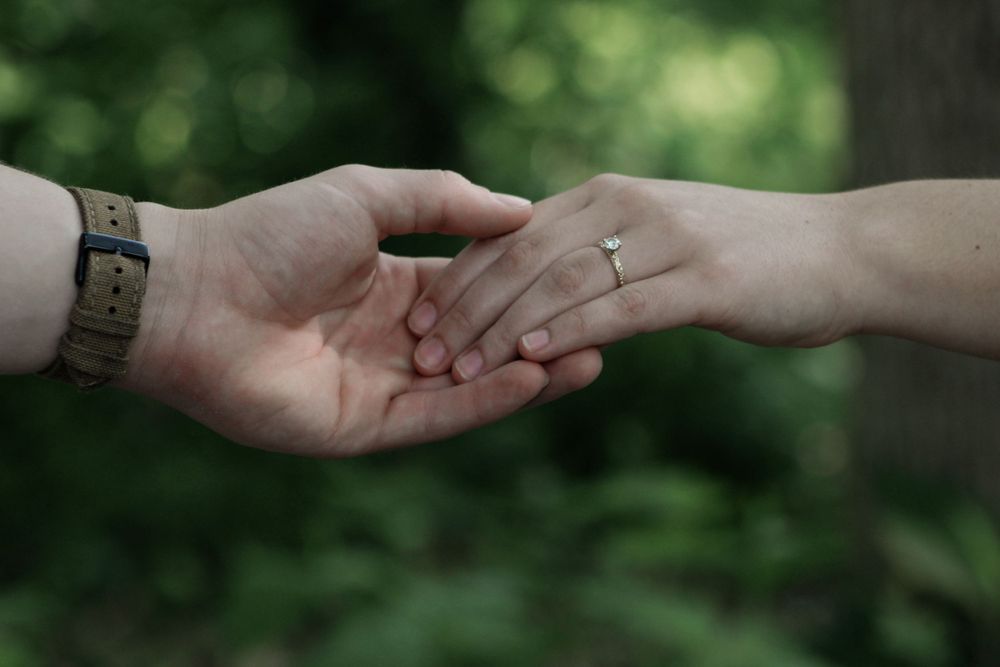 Two hands reaching out to touch in a tender moment against a blurred green background.