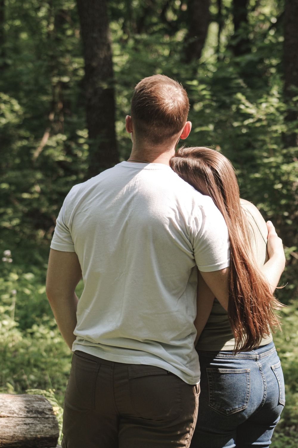 Two people sit close together on a log in a peaceful forest setting.