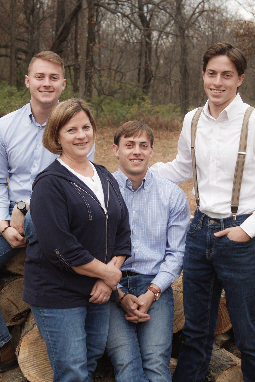 Young people in coordinated outfits of suspenders and button-downs sitting on wooden logs outdoors.