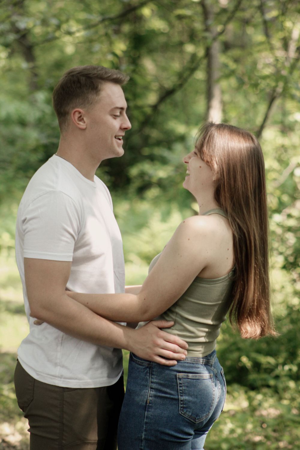 Couple sharing an embrace during outdoor photo session with forest backdrop.
