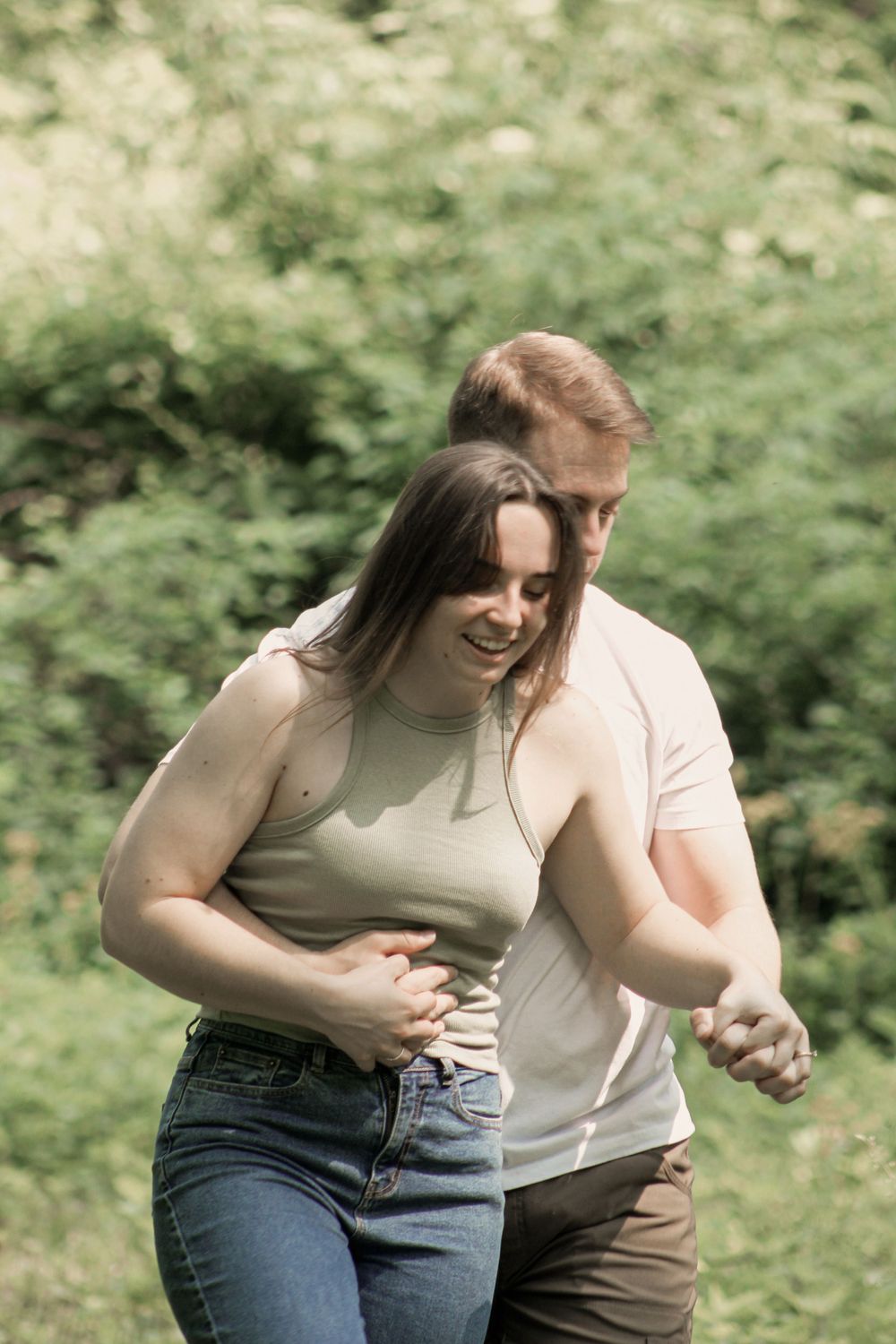 Two people share a playful dancing moment in a sunlit forest clearing.