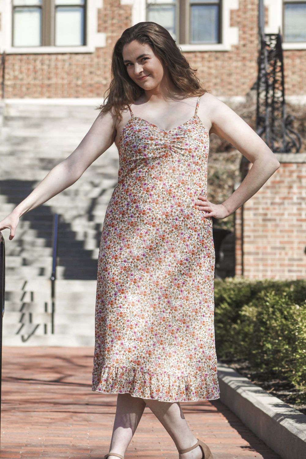 A floral dress is showcased in a series of poses on a brick patio.