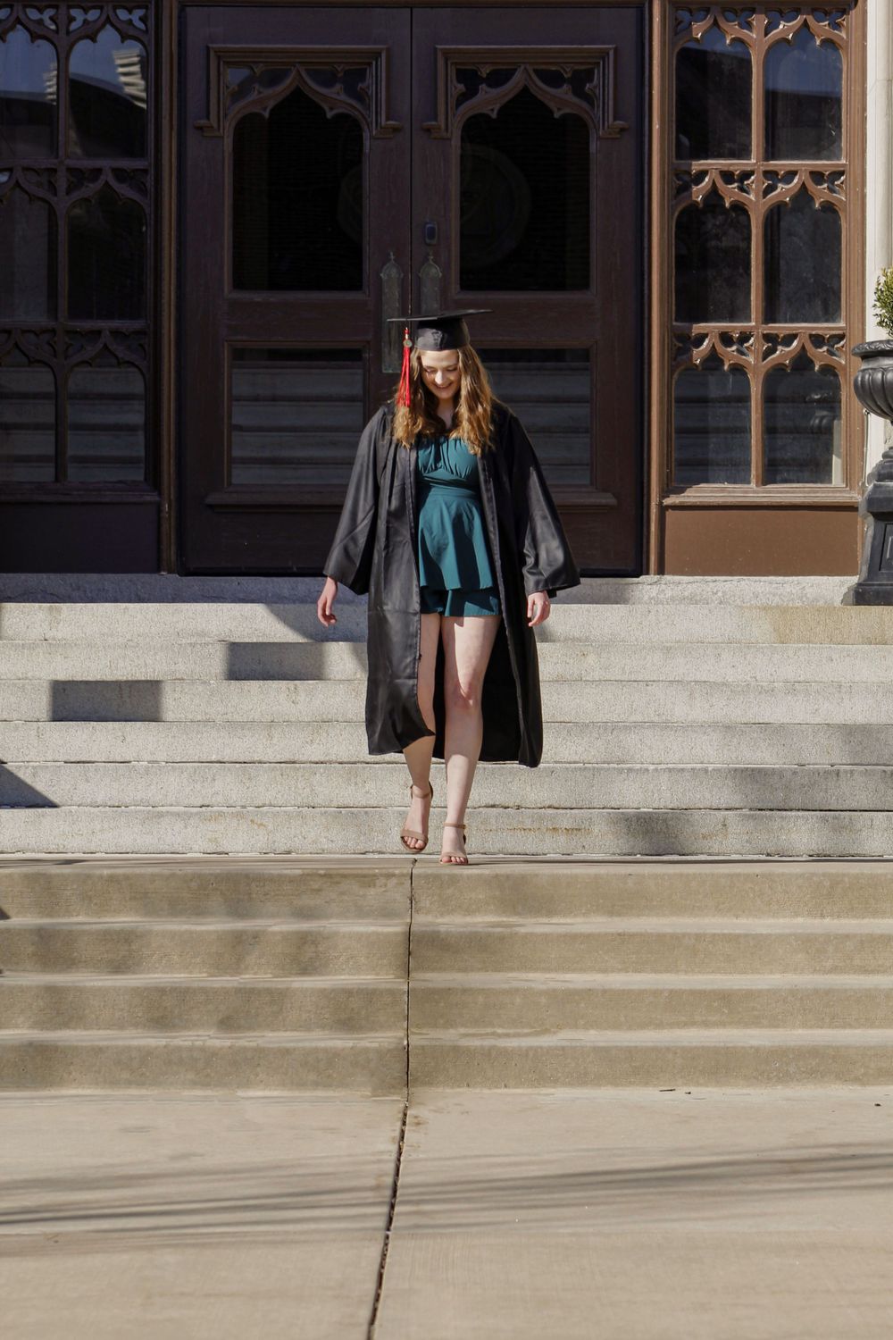 Graduate in academic dress walking down concrete steps of historic building.