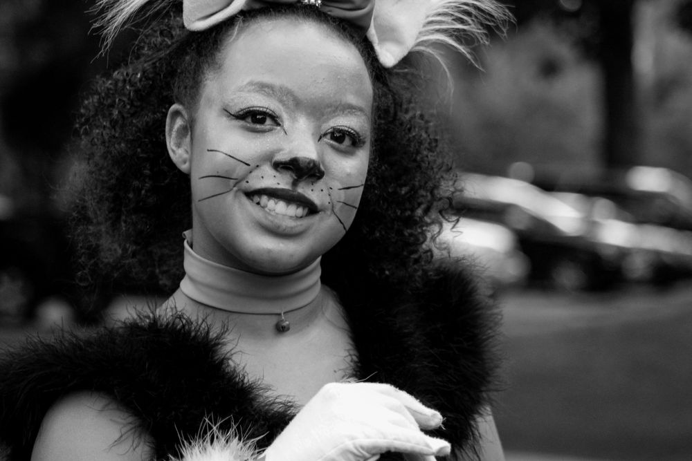 A black and white portrait showing whimsical face paint and feathered accessories.