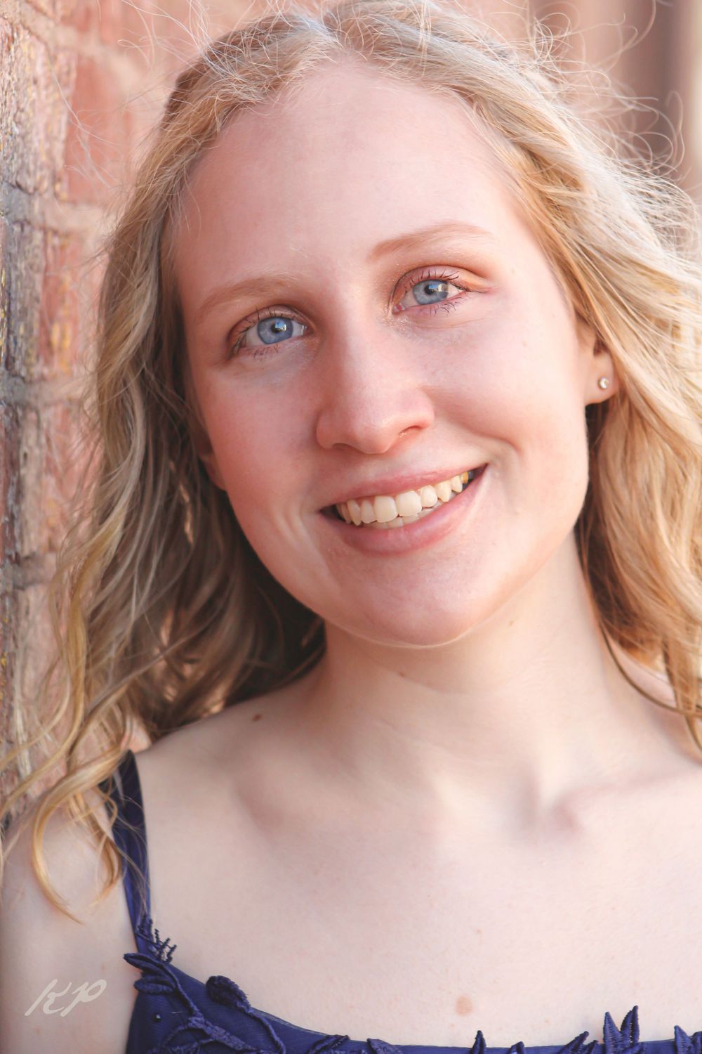 Portrait against brick showing natural makeup and navy blue dress details.