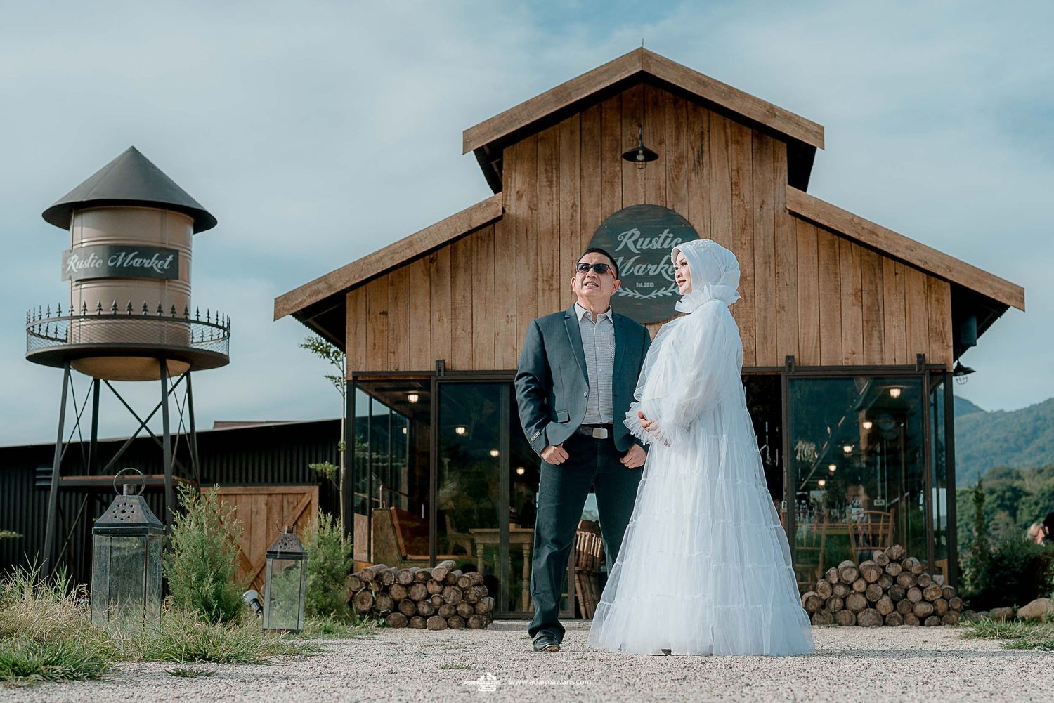 Wedding couple standing in front of wooden barn with clock tower in mountain setting.