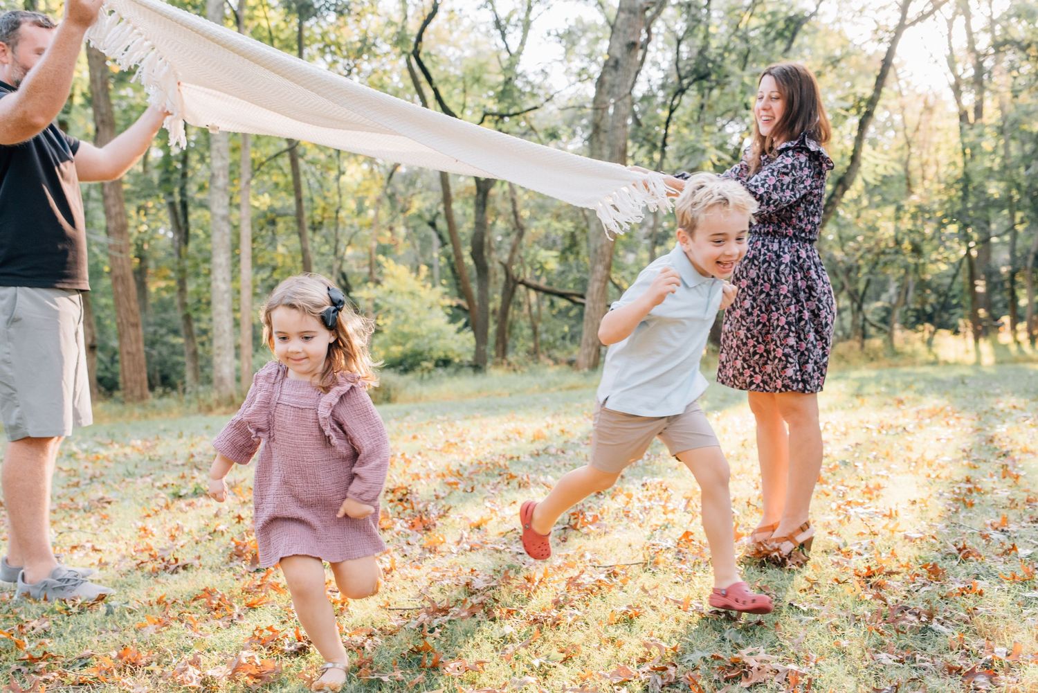 Kids run under a white blanket playing in the park.