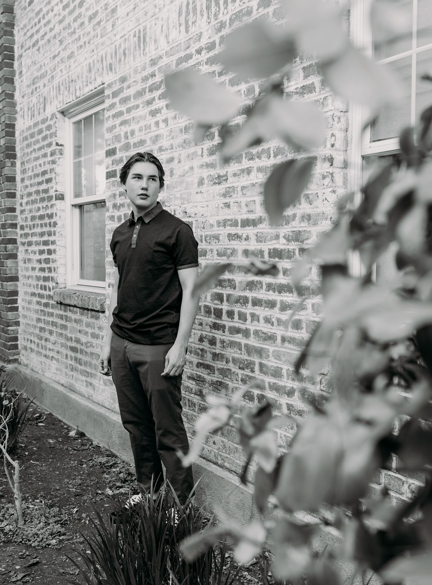 Guy standing with hands in pockets, in front of a brick wall looking.