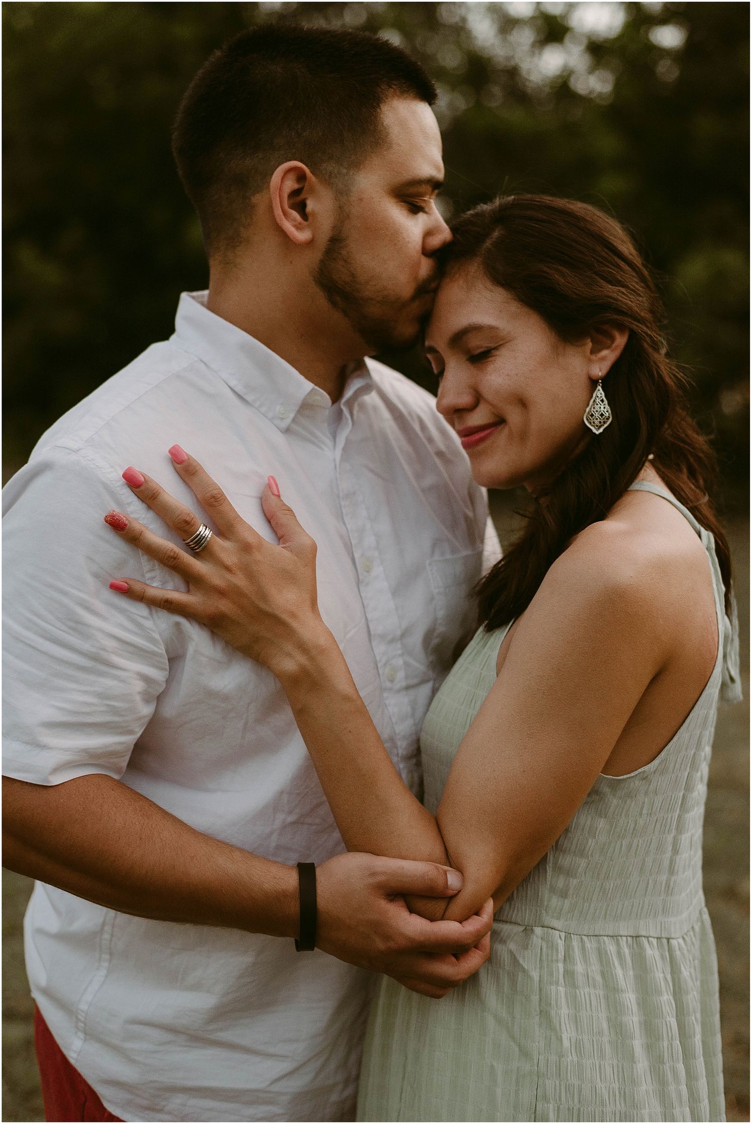 Romantic couple embraces in warm sunset light as she shows off her ring in a tender outdoor moment.