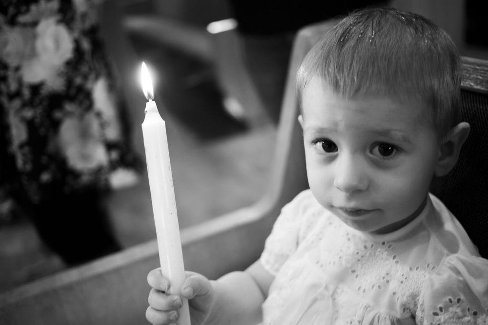 A white candle glows brightly in a dimly lit room.