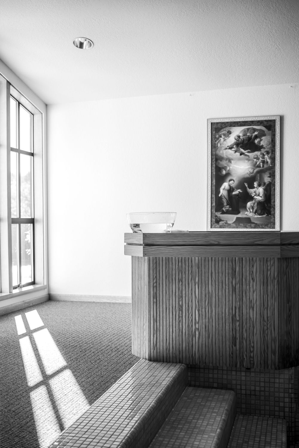 Black and white interior of a church with sunlight streaming through windows and a religious painting on the wall.