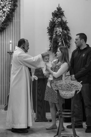 Religious ceremony with priest and family members by decorated Christmas tree.