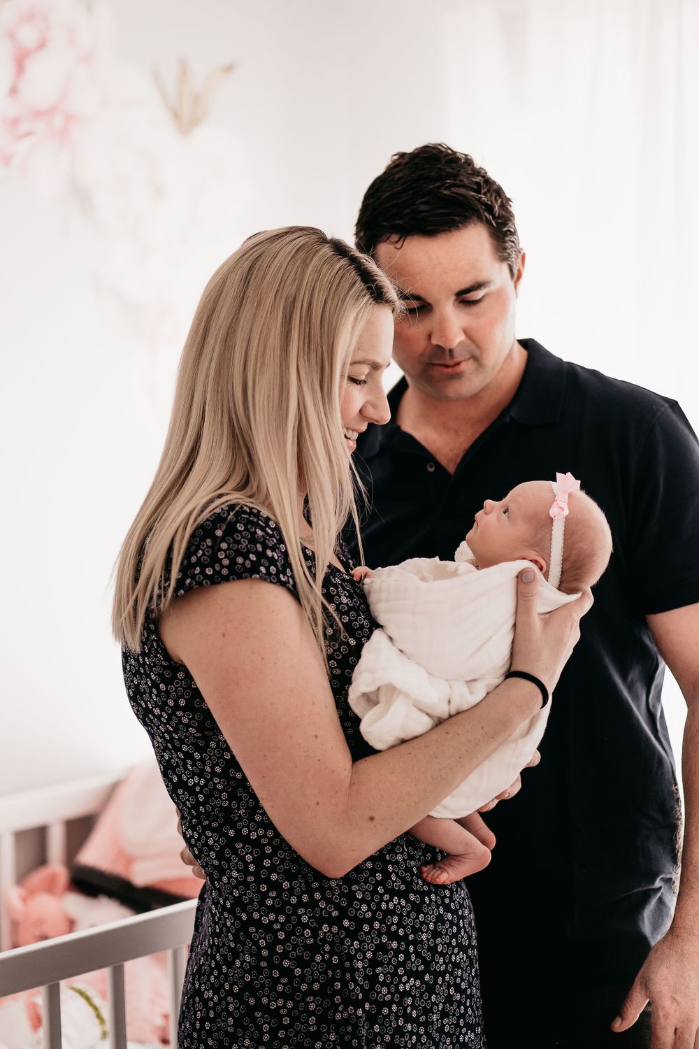 A couple shares an intimate moment while holding their newborn baby in a nursery setting.