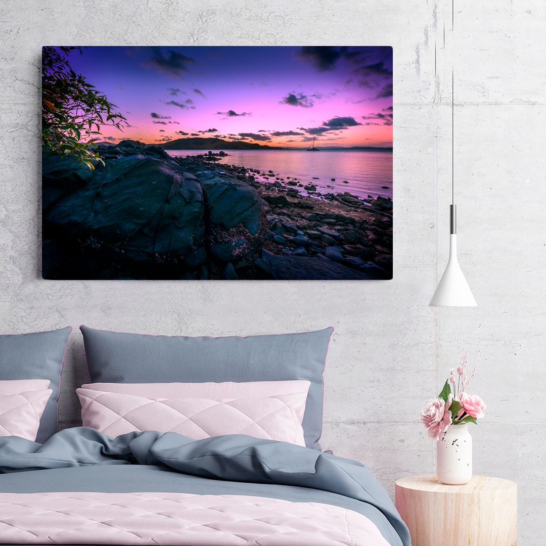 Dramatic purple and pink sunset over a rocky coastline with silhouetted trees and calm ocean waters.