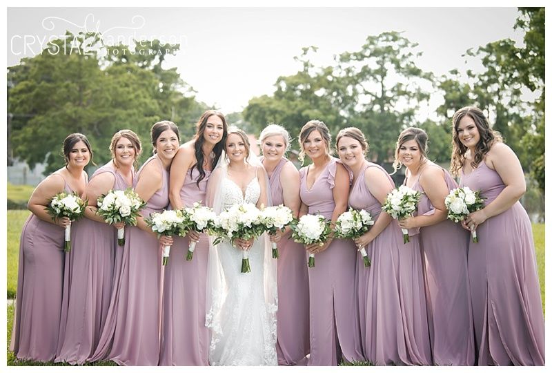 Bridesmaids in dusty purple dresses holding bouquets outdoors.
