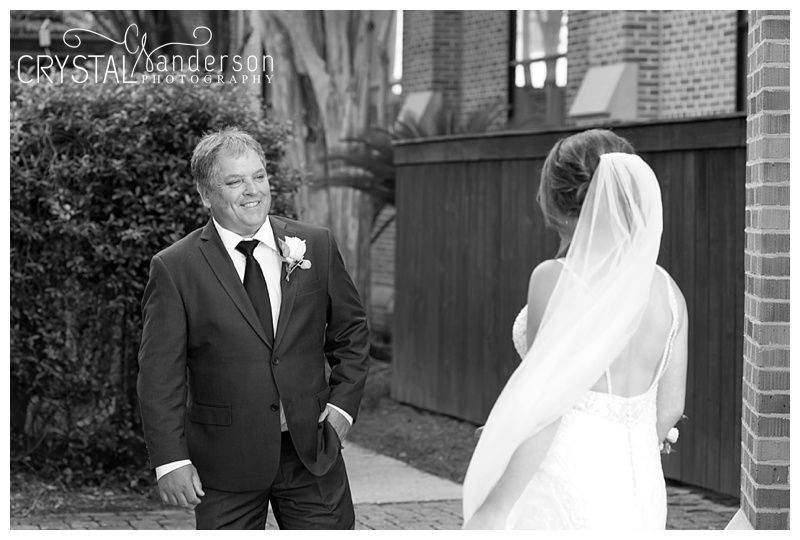 Black and white wedding portrait showing a tender moment between the couple against a brick wall backdrop.