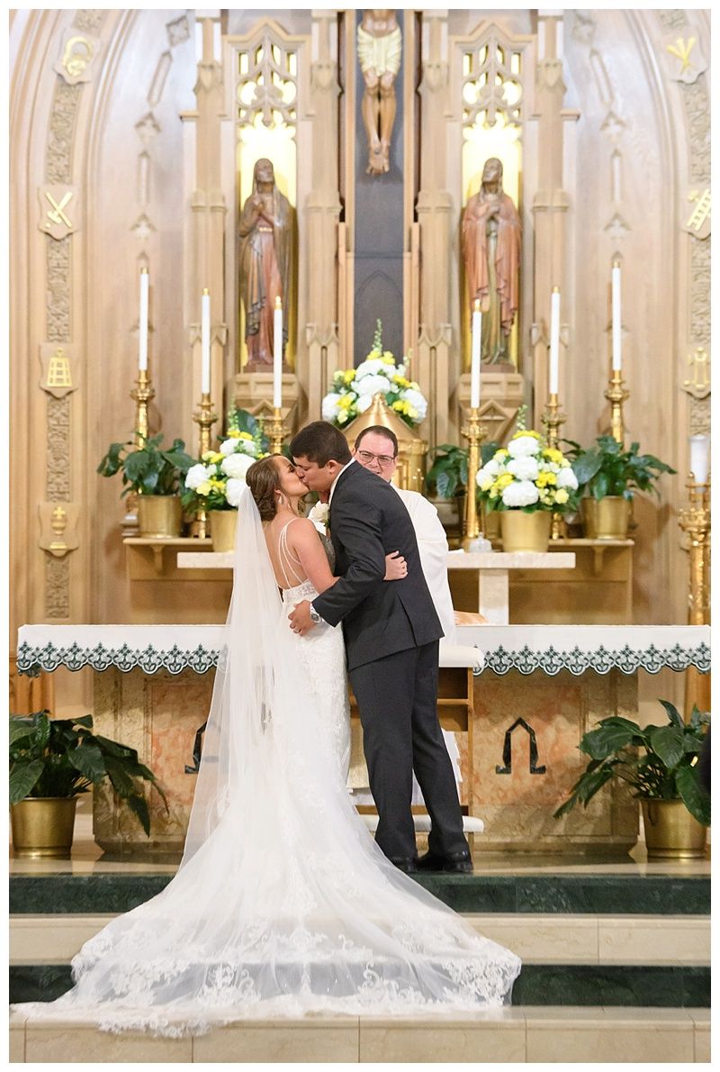 Romantic wedding couple shares intimate moment at ornate church altar with white floral arrangements and candles.