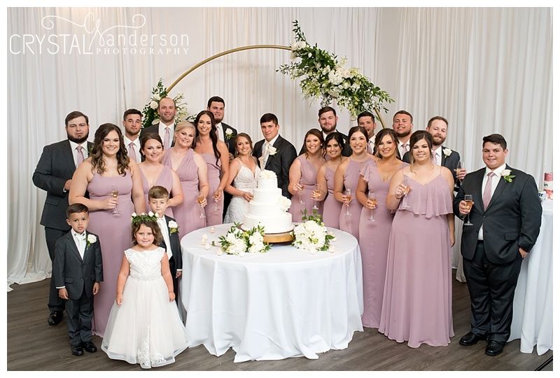 Wedding party and guests gathered in reception hall with pink bridesmaid dresses and white decor.