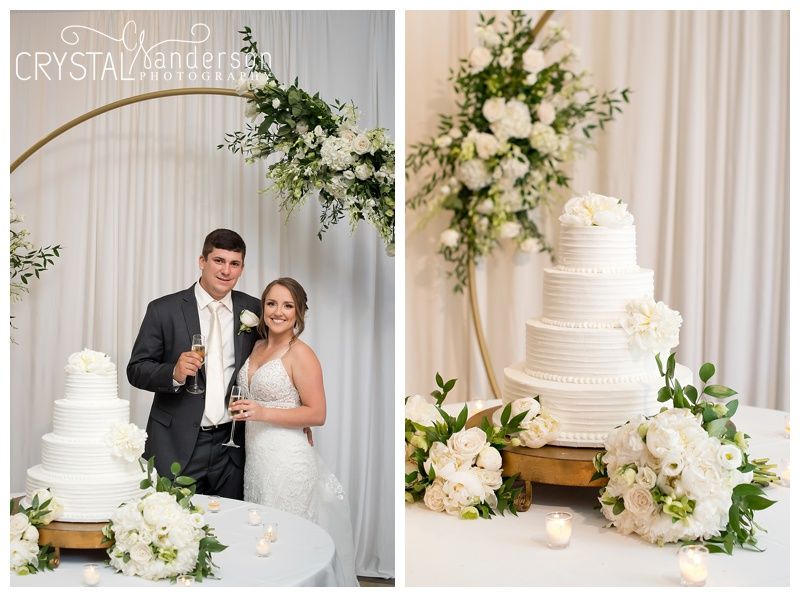 Elegant white wedding cake display with floral decorations and gold hoop backdrop.