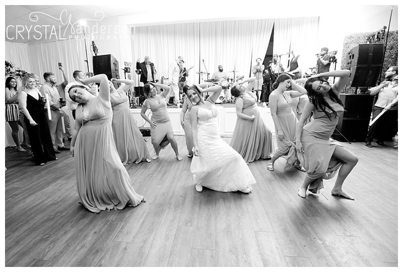 Black and white photo of wedding guests dancing in a line formation at a reception.