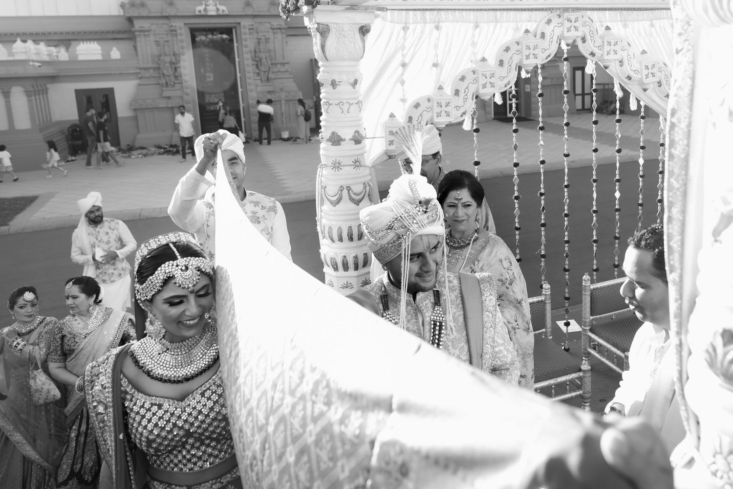 A black and white photograph showing a traditional Indian wedding ceremony with ornate decorations and flowing fabrics.