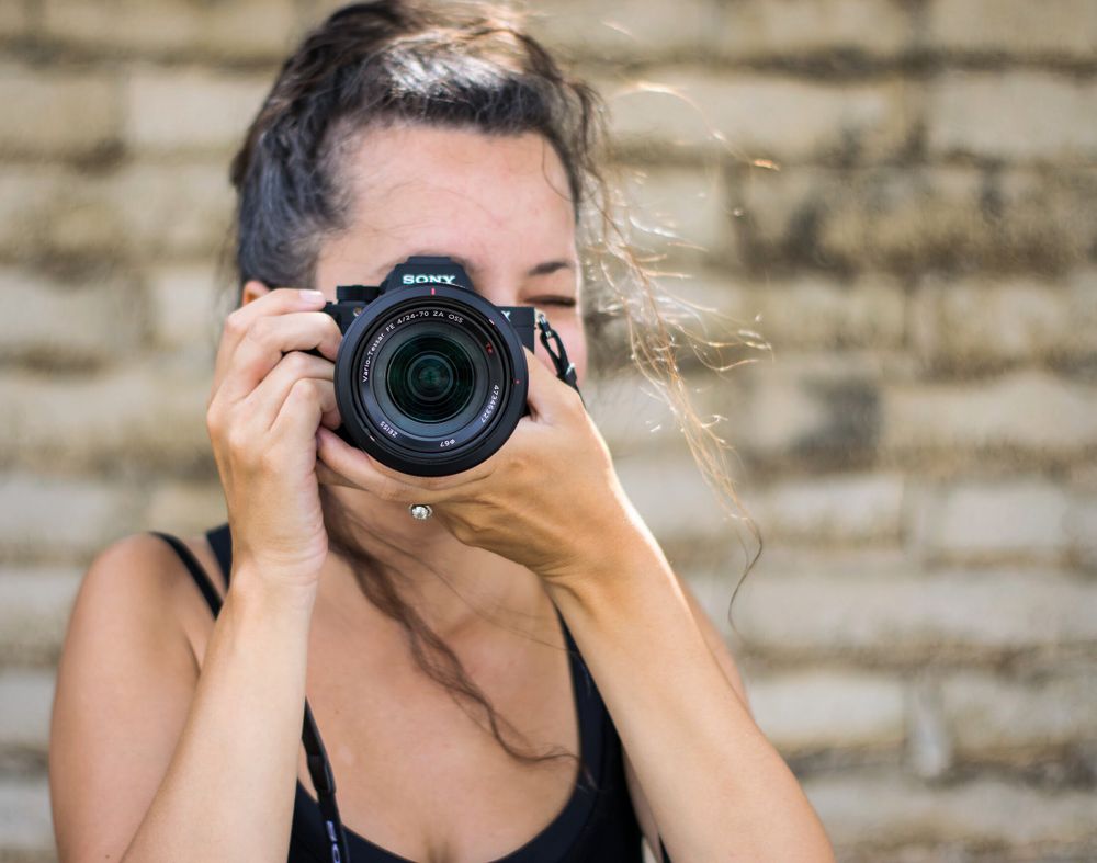 Close-up of photographer using professional DSLR camera against stone wall.