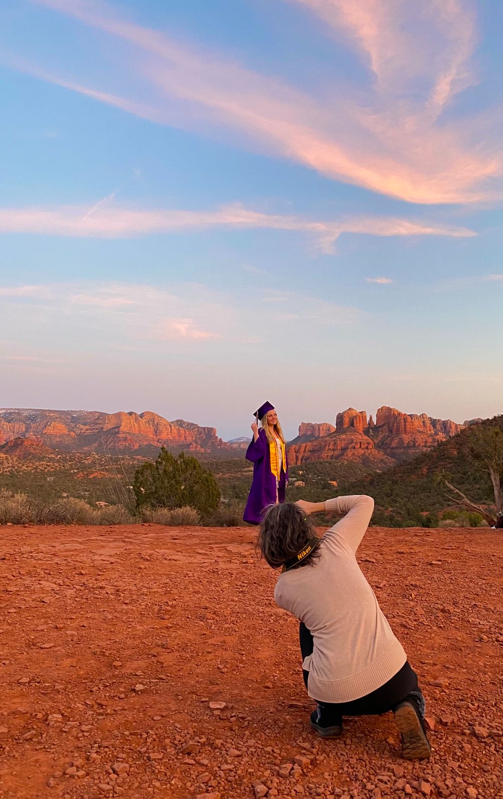 Photographer capturing subject in purple dress against red rock landscape at sunset.