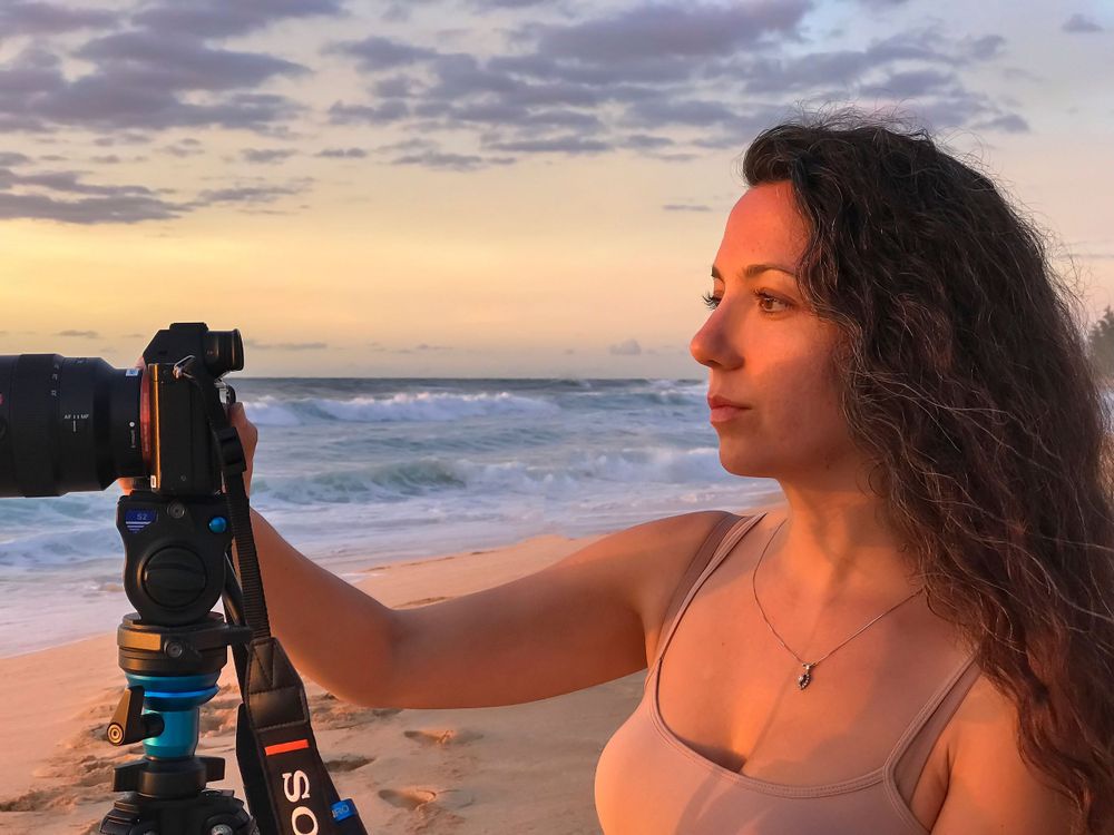 Photographer works with camera equipment on beach during golden hour sunset.