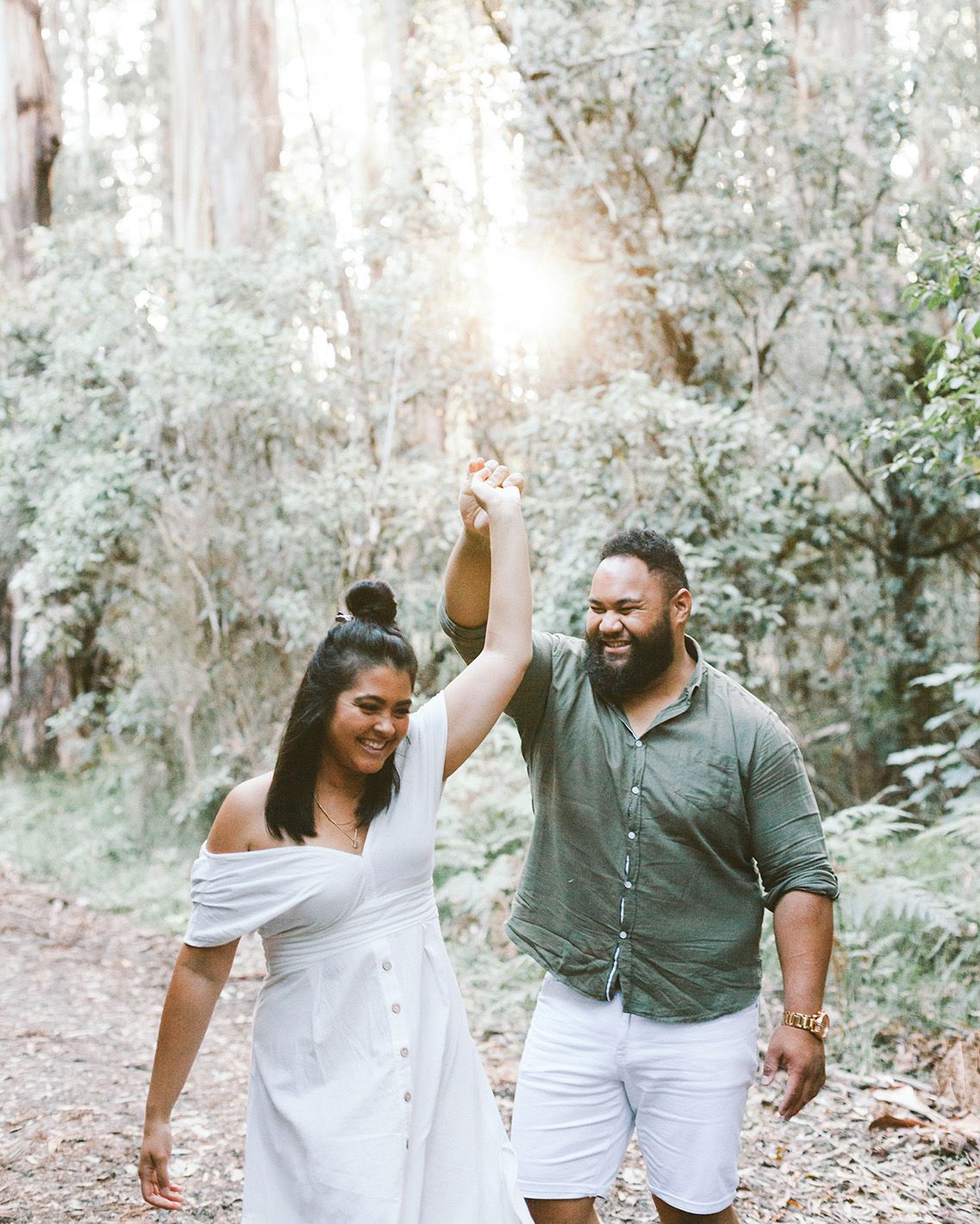 A joyful couple dancing together on a sunlit forest path in casual attire.