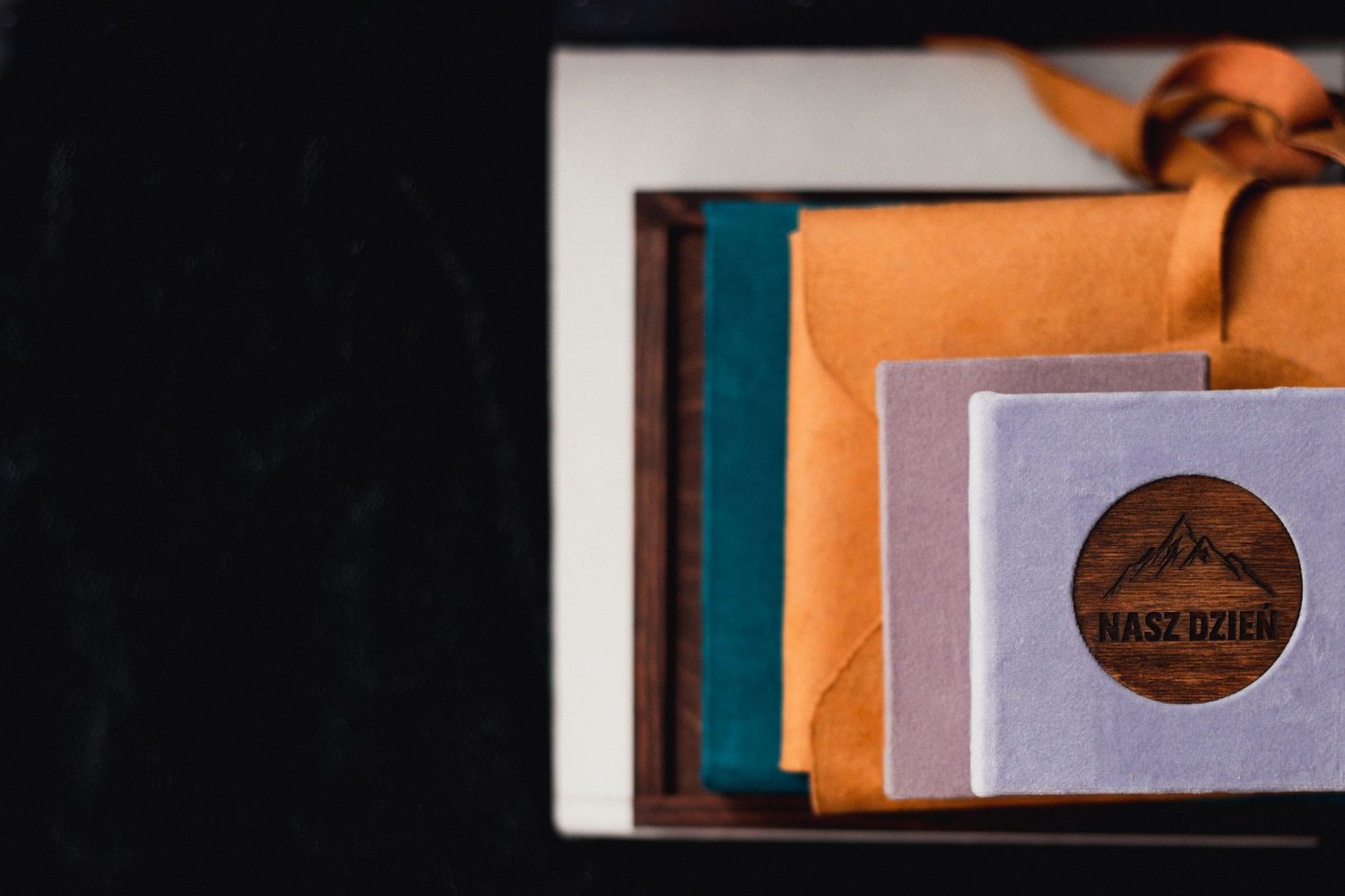 Wedding photography album with white and orange packaging displayed on dark surface.