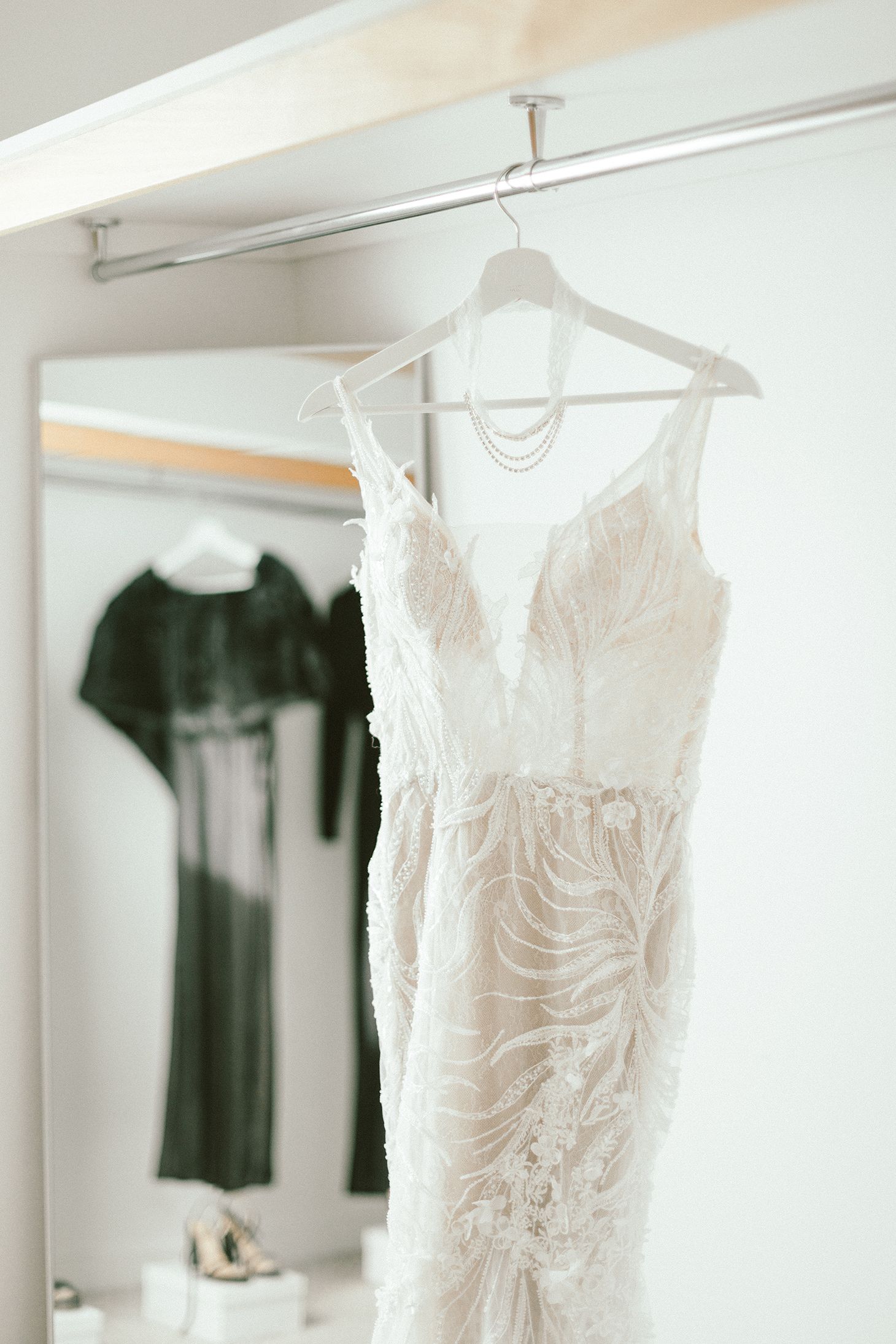 Detailed lace wedding dress with plunging neckline hanging on white hanger against light wall.