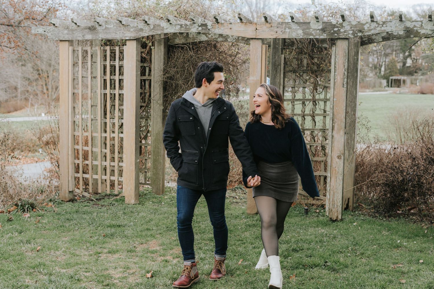 Couple walking together through garden archway during casual photoshoot.