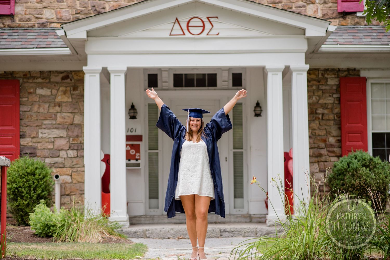 Graduate celebrates in front of sorority house with Greek letters and white columns.