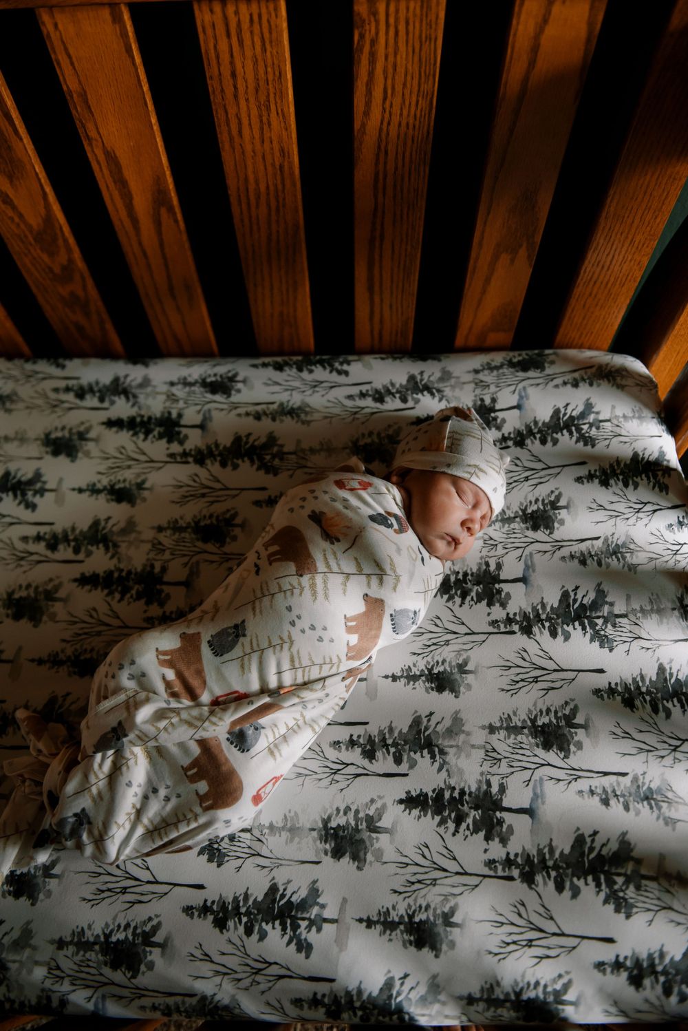 Newborn baby sleeping peacefully on a patterned white bedsheet in a wooden crib.