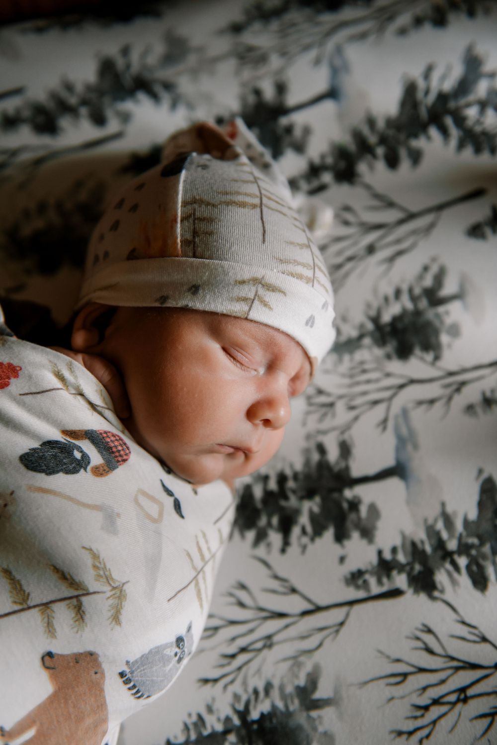Baby wearing white clothing and cap rests on a patterned sheet.