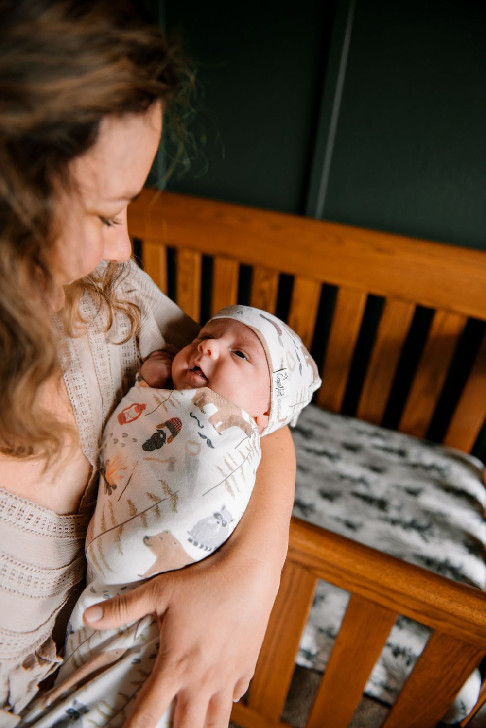 Gentle nurturing moment beside wooden crib with patterned bedding.