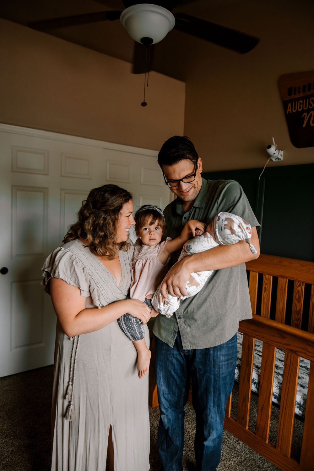 Family gathering around wooden crib in dimly lit nursery.