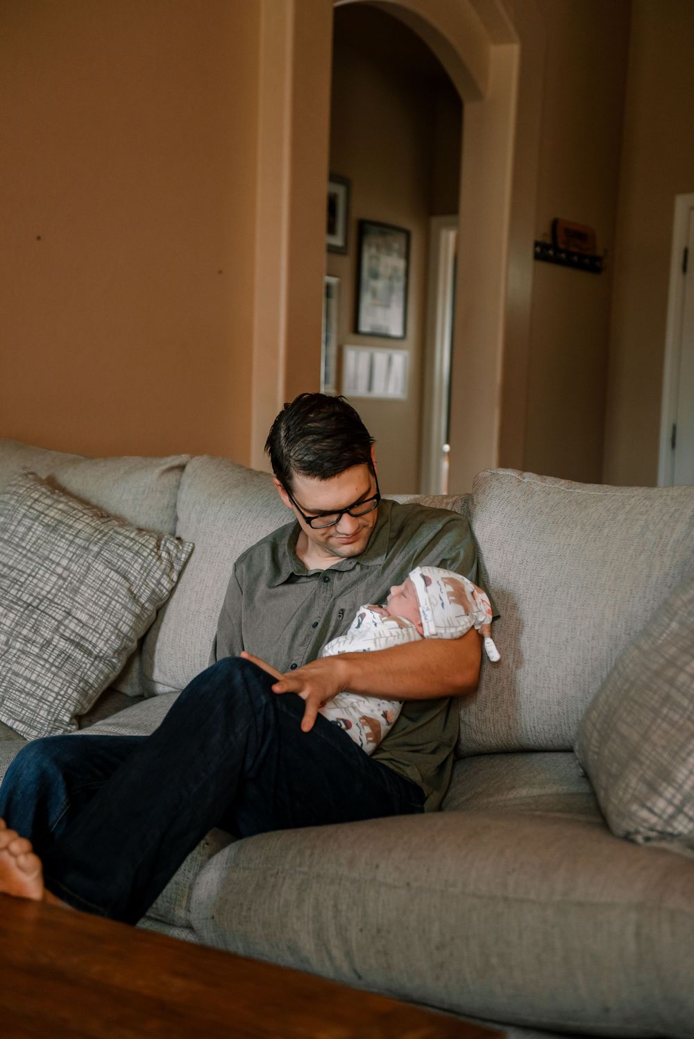 Parent resting on a comfortable gray couch while holding a sleeping infant.