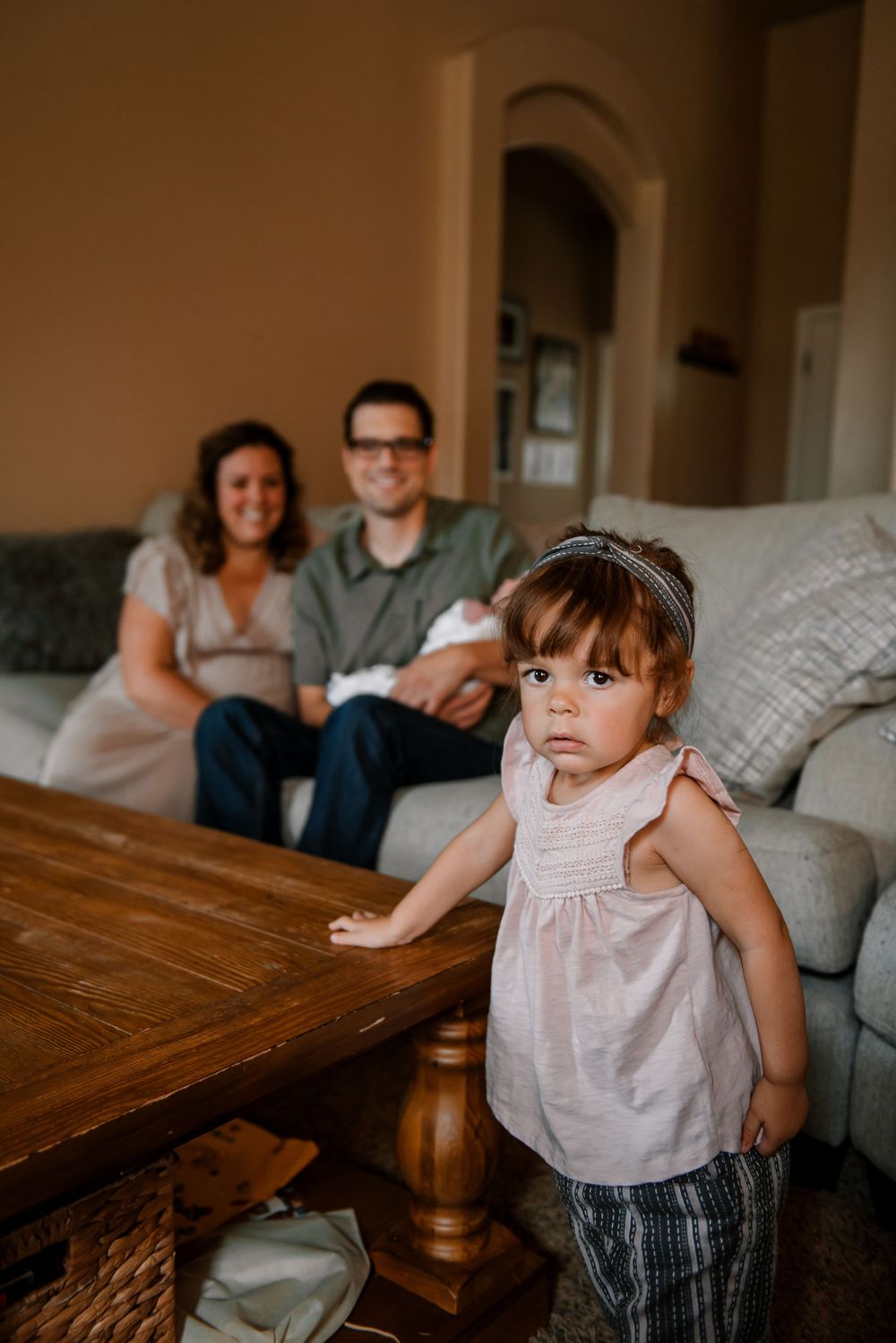 Family relaxing together on a cozy gray couch with a wooden coffee table in a warm-toned living room.
