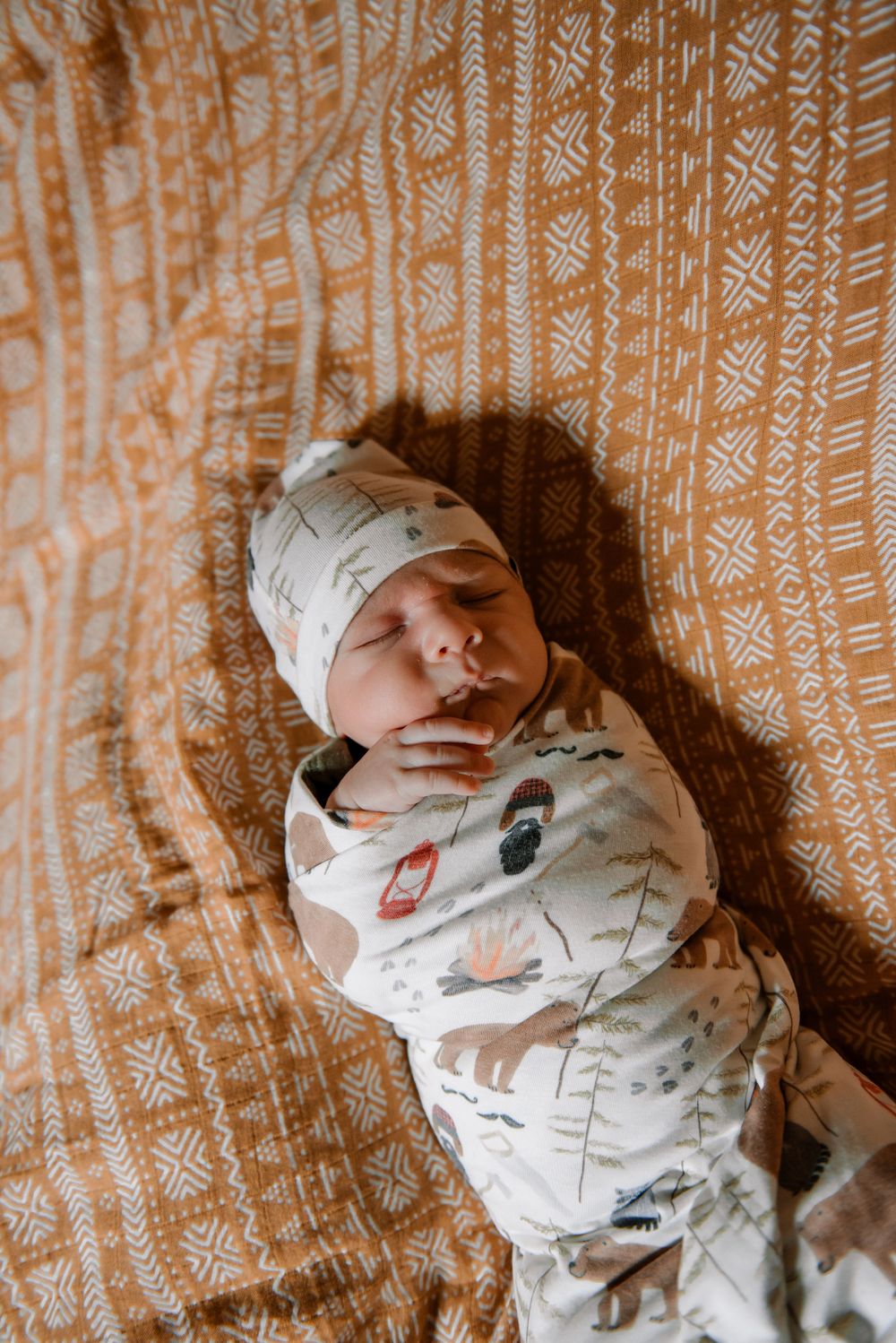 Newborn baby wearing a white patterned onesie lying on a textured orange blanket.