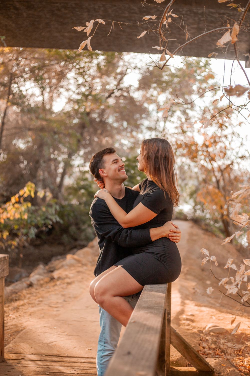 Romantic couple embracing on wooden bridge during autumn surrounded by fallen leaves.