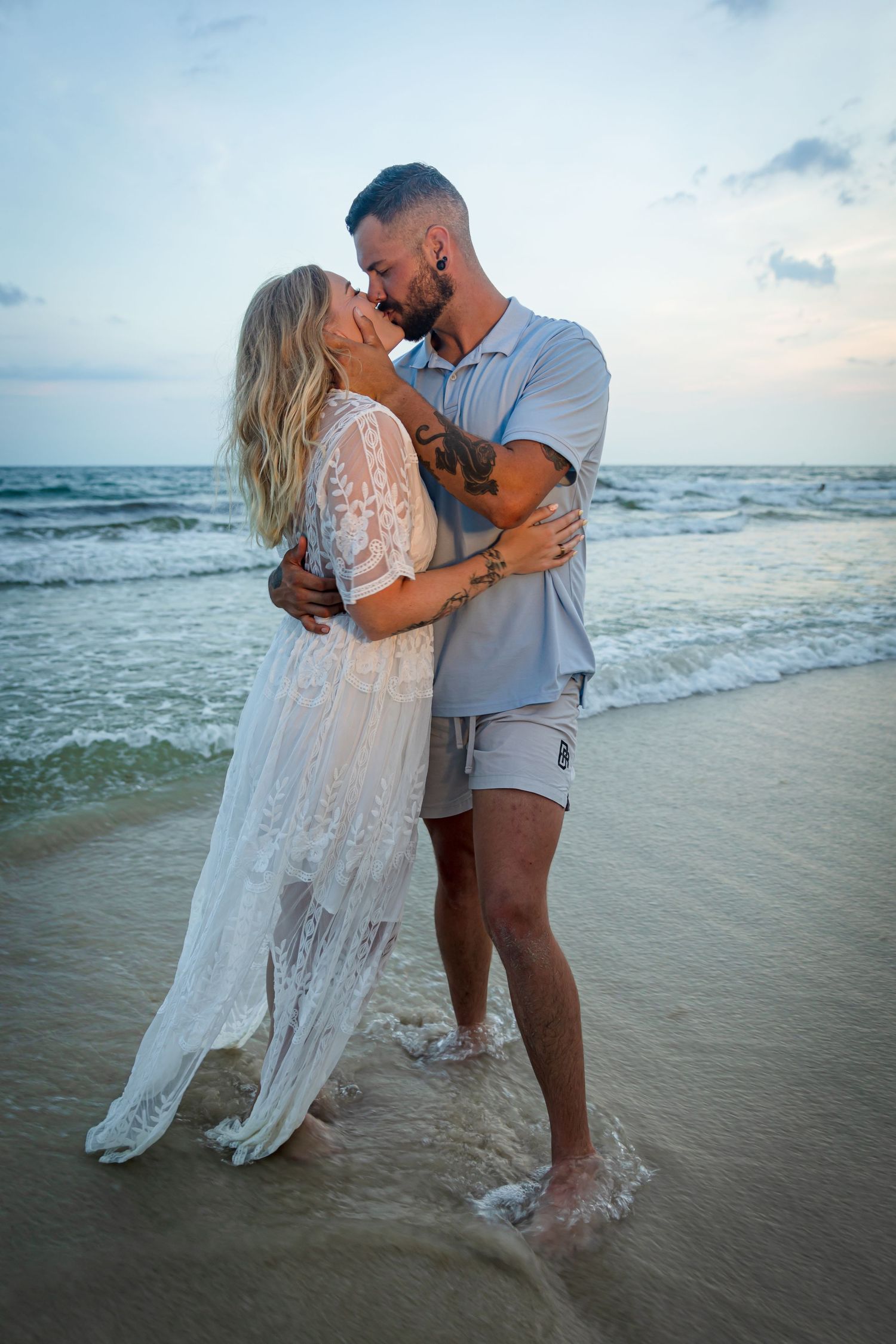 Romantic beach scene at sunset with couple embracing in the ocean waves.