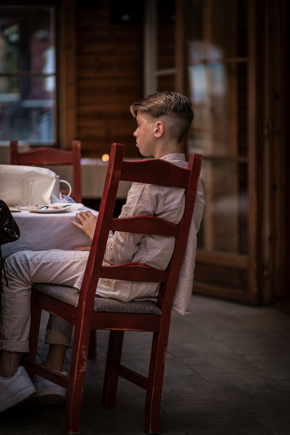 A young guest sits in a wooden chair at a wedding reception table.
